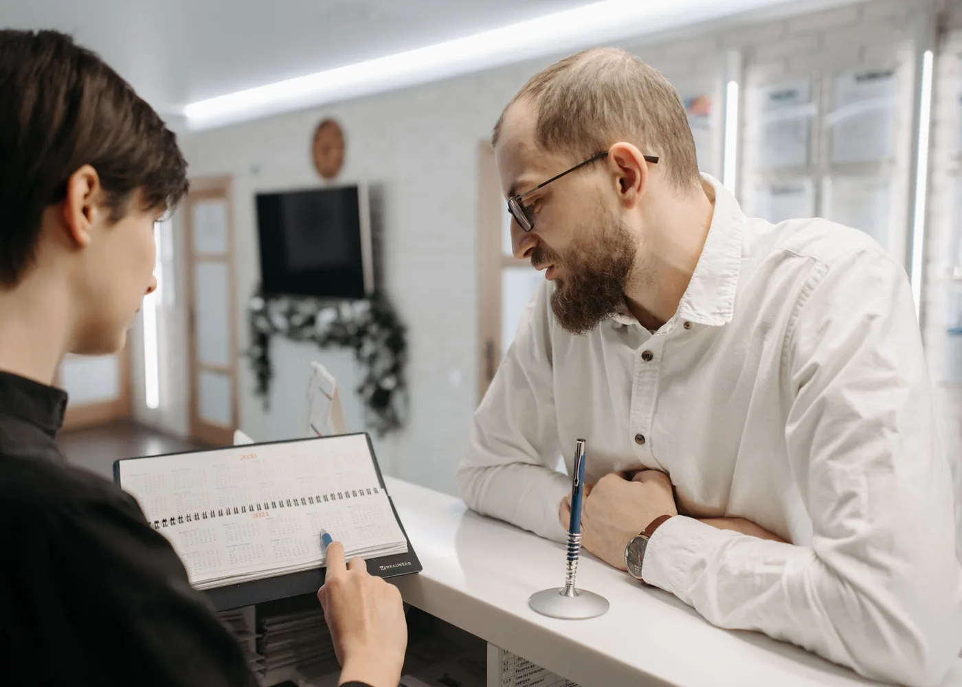 A receptionist checking the appointment book with a patient at the desk