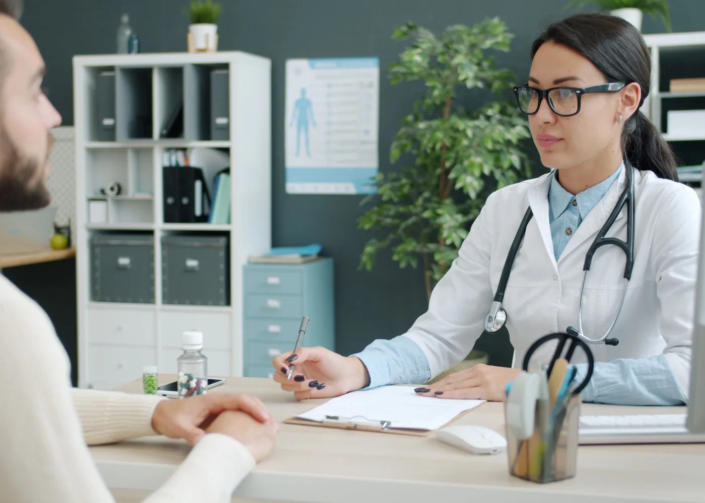 A doctor taking notes while a patient talks her through his symptoms